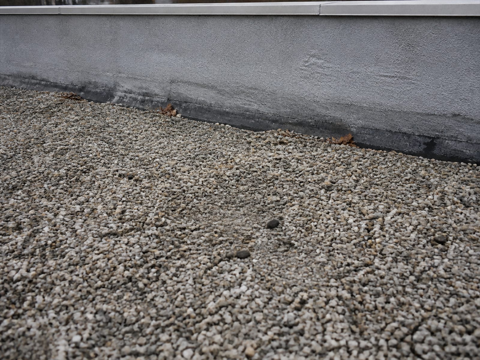 Loose roof gravel meeting the base of a low parapet wall